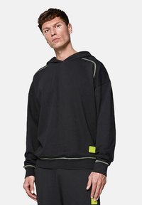 Czarna bluza z kapturem, z zielonymi przeszyciami i limonkową metką z przodu. Wykonana z miękkiego, strukturalnego materiału.