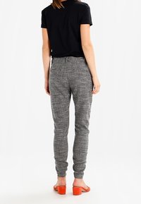 Pantalon de jogger gris texturé avec une coupe fuselée, des poignets élastiques aux chevilles et des poches, associé à un t-shirt noir et des sandales à talons blocs orange.