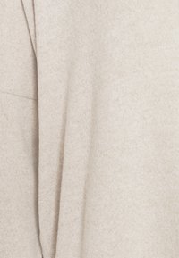 Tissu beige clair avec un tissage doux et texturé. Présente un design drapé avec des variations subtiles de teinte et de couleur, créant une apparence chaleureuse.