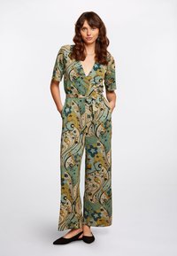 Mono floral en verde y beige, con un profundo escote en V, mangas cortas, cintura ceñida con cinturón y piernas anchas con patrones intrincados.