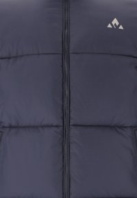 Gilet matelassé bleu marine avec une fermeture éclair verticale, offrant des sections matelassées et un logo dans le coin supérieur. Texture lisse et design isolé.
