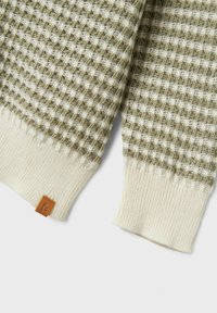 Zeleno-biely pletený sveter s textúrovaným kockovaným vzorom, rebrovanými krémovými manžetami a malou hnedou koženou značkou.