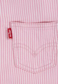 Tissu rayé rose et blanc avec une poche arrière cousue et une petite étiquette rouge. Texture lisse et design en denim classique.
