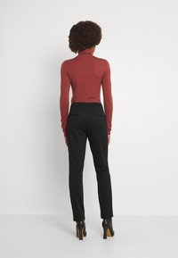 Punainen korkeakauluksinen neule yhdistettynä mustiin istuviin housuihin, joissa on sileä pinta. Korkokengät ovat mustat, joissa on puisia yksityiskohtia.