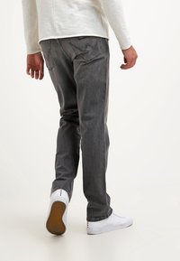 Grå denimjeans med rak passform, med en minimalistisk design och subtila sömmar. I kombination med vita sneakers mot en ljus bakgrund.