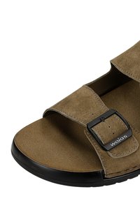 Hnědý semišový sandál s otevřenou špičkou, černým nastavitelným páskem se sponou označenou "wojas" a černým okrajem podrážky.