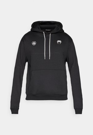 Crna pulover majica s kapuljačom s kangaroo džepom, bijelim korsetama i dva logotipa na prsima. Izrađena od mekog, teksturiranog materijala.