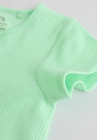 Petit haut pour bébé à manches courtes côtelé vert menthe doux avec un col rond, présenté à plat sur une surface blanche.