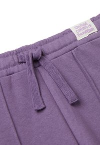 Primo piano di un elastico dei pantaloni della tuta viola con cordino e etichetta bianca che recita "United Colors of Benetton" in un font lilla.