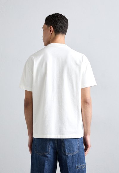 Camiseta de algodón blanca de manga corta, con un corte relajado y un escote redondo, combinada con pantalones de mezclilla azul. Textura suave, sin patrones visibles.