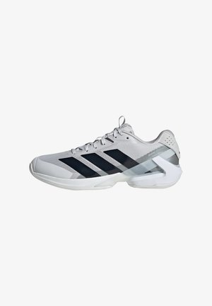 Scarpa sportiva grigia e bianca con strisce nere, lacci e un supporto rigido geometrico per il tallone su sfondo bianco.