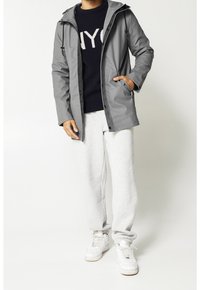 Grå vattentät jacka med huva, dragkedja och framfickor, som bärs över en marinblå tröja och grå sweatpants, kombinerad med vita sneakers.