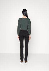 Green knit sweater and black skinny jeans. The sweater has a round neckline and long sleeves, while the jeans feature a smooth texture and slim fit.