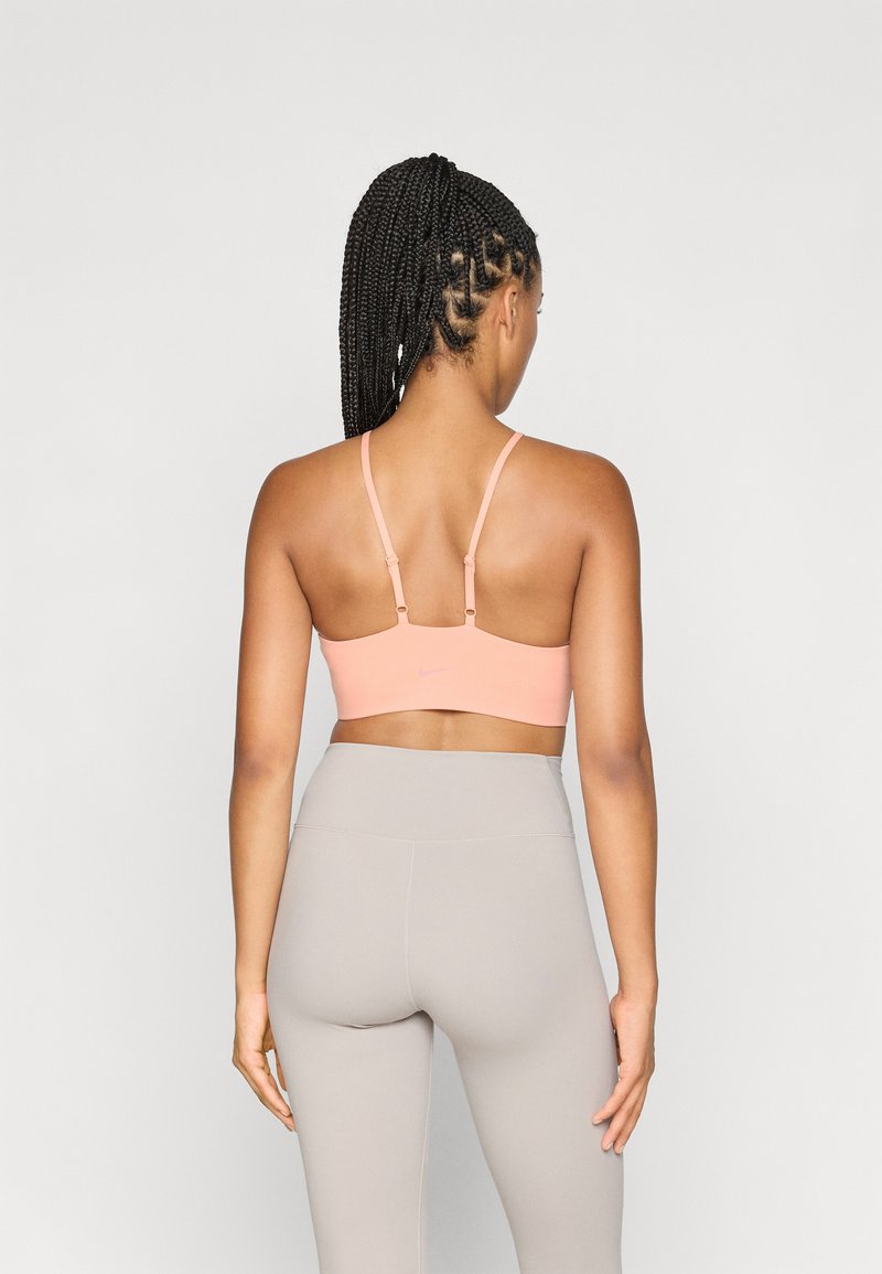 Sport-BH in zartem Rosa mit verstellbaren Trägern, glatter Textur und minimalem Branding. Kombiniert mit hellgrauen, hochgeschnittenen Leggings.