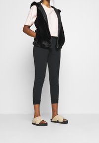 Black faux-fur vest, light pink cropped t-shirt, black fitted pants, and beige cross-band sandals with black soles.