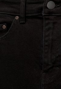 Tissu en denim noir d'un jean montrant un gros plan sur la poche avant, les rivets en cuivre et les détails de couture visibles.