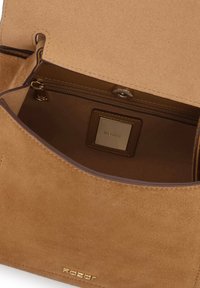 Ruda suede rankinė su lygaus paviršiaus tekstūra, turinti užtrauktuko skyrių ir stačiakampį logotipo žymeklį viduje. Papuošta tamsiomis siūlėmis.