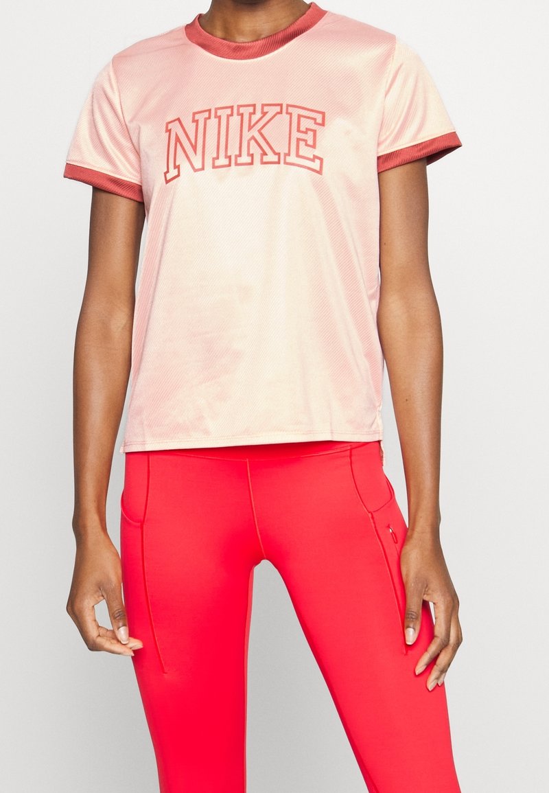 Person som bär en ljusrosa Nike-t-shirt med röda detaljer och klara röda åtsittande träningsleggings mot en neutral bakgrund.