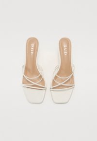 Sandales à talons blancs avec un orteil carré, dotées de délicates lanières croisées. La semelle intérieure est de couleur beige clair avec "RAID" imprimé.