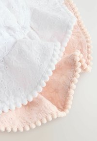 Valkoinen ja vaaleanpunainen puuvillakangas kukkakuviolla, jossa on tekstuuriset pom-pom-reunat pehmeässä väripaletissa.