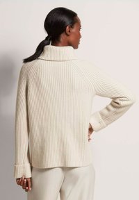 Cremfarbener gerippter Pullover mit hohem Kragen und langen Ärmeln, der eine lässige Passform und umgeschlagene Bündchen aufweist. Strukturiertes Strickdetail durchgehend.