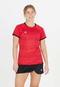 Punainen lyhythihainen urheilupaita, jossa on teksturoitu kuosi ja mustat yksityiskohdat, yhdistetty mustaan hameeseen. Kangas näyttää kevyeltä ja hengittävältä.