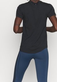 Černé tričko s krátkým rukávem a kulatým výstřihem, volného střihu, spárované s modrými legínami se postranními pruhy.