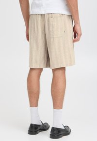 Shorts rayés beiges en tissu léger, dotés d'une poche arrière et d'une taille élastique, associés à des chaussures noires et des chaussettes blanches.