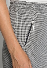 Pantaloni houndstooth nero e bianco con vita elastica e tasca con zip, caratterizzati da hardware argentato elegante.