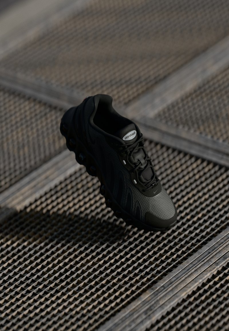 Scarpa sportiva nera con superiore texturizzato, design curvo e lacci visibili. Elementi di ammortizzazione rotondi ben evidenti nella suola.