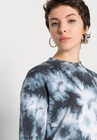 Sweatshirt de algodão com um padrão tie-dye azul e preto, gola redonda tradicional e punhos canelados para textura e ajuste.