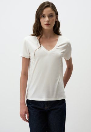 Witte T-shirt met korte mouwen en V-hals, gemaakt van gladde stof. Het heeft een relaxte pasvorm en wordt gedragen met een donkere spijkerbroek.