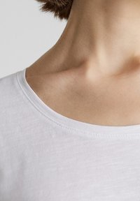 Witte katoenen T-shirt met een ruime halslijn, en een soepele textuur en schone randen, weergegeven op een neutrale achtergrond.