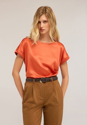 Satin orange top with short rolled sleeves, paired with high-waisted brown trousers and a black belt featuring a gold buckle.
