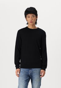 Suéter de punto negro de manga larga con cuello redondo y dobladillo acanalado. Combinado con unos jeans azul claro, con una textura suave y un diseño ajustado.