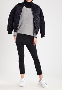 Granatowa pikowana kurtka typu bomber, szary sweter dziany, czarne zwężane spodnie z białymi paskami, białe trampki z subtelnymi akcentami. Prosty i nowoczesny design.