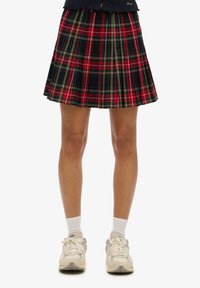 Plaid mini skirt in black, red, and yellow with knife pleats. Worn with white ankle socks and multi-colored sneakers.