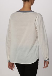 Blusa bianca leggera e semi-trasparente con maniche lunghe, rifiniture blu sul colletto, polsini con bottoni e orlo arrotondato. Progettata per un look casual.