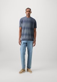 Kortermet strikket genser med gradient blå farge, rund hals og ribbestrikket hem, kombinert med lyseblå rette jeans og beige slip-on sko.