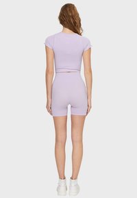 Top corto lila y pantalones cortos de talle alto a juego, hechos de una tela elástica, con un diseño ajustado y mangas cortas. Incluye zapatillas blancas.