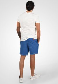 Weißes T-Shirt mit kurzen Ärmeln und blaue Baumwollshorts mit umgeschlagenen Säumen, ausgestattet mit einer Gesäßtasche und einem kleinen Akzent aus braunem Leder.