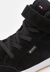 Mustad musta sametise pealsetega kõrge kvaliteediga sneaker, millel on võrgust keel, nööridega sulgemise disain, Velcro rihm ja GORE-TEX silt. Omab valget kummist tallat.