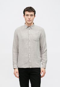 Svetlosivá košeľa na gombíky z text�úrovanej tkaniny, s jedným náprsným vreckom a štandardným golierom. Pod ňou čierne nohavice.