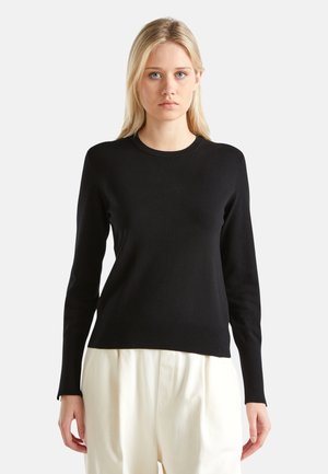 Pull en tricot noir à manches longues avec col rond et ourlet côtelé, fabriqué dans un tissu lisse, associé à un pantalon blanc à jambes larges.