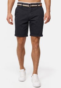 Shorts en coton marine avec des ourlets retroussés, associés à une ceinture rayée multicolore et des baskets blanches. Texture lisse, design décontracté.