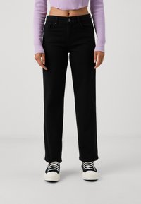 Black high-waisted straight-leg jeans with five pockets, belt loops, and metal button closure, paired with black and white sneakers.