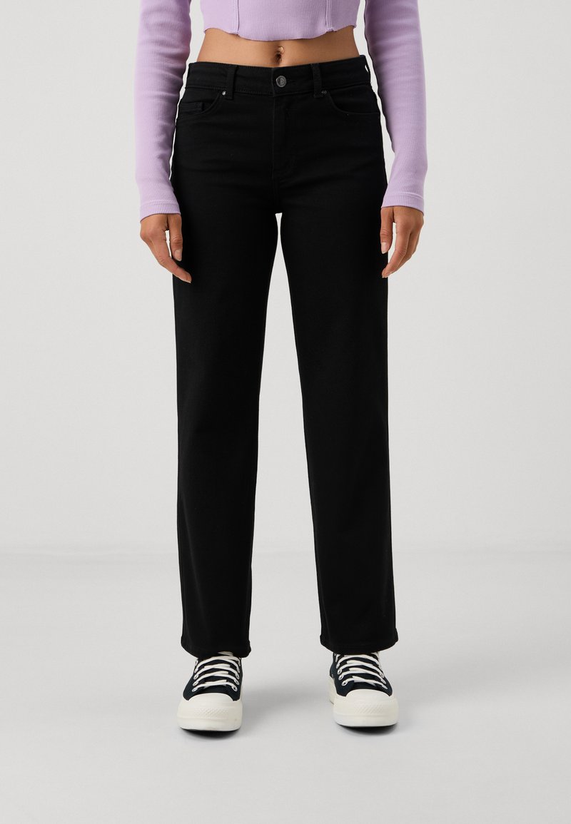 Black high-waisted straight-leg jeans with five pockets, belt loops, and metal button closure, paired with black and white sneakers.