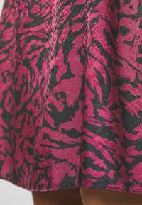Jupe à motifs fuchsia et noirs avec un tissu texturé, présentant un design fluide et des détails visibles sur l'ourlet.