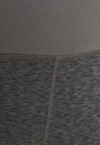 Primer plano de una tela bicolor con la sección inferior de un gris oscuro jaspeado y la sección superior de un gris oscuro sólido con relieve, unidas por costuras visibles.