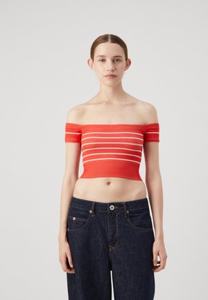 Punane õlgadelt maha libisev lühike topp valgete horisontaalsete triipudega. Valmistatud ribakanga materjalist. Ühendatud tume denim kõrge vöökohaga teksapükstega.